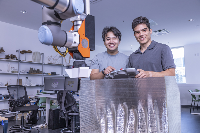 Two student smiling while using a 3D printer