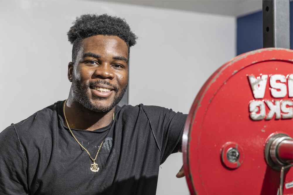 Male student smiling next to a barbell