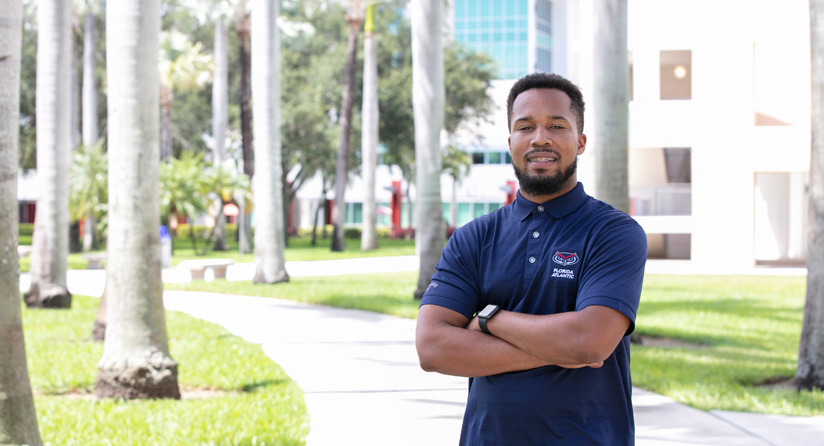 Male student standing outside next to palm trees