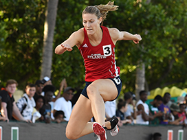Female track member jumping over a hurdle.